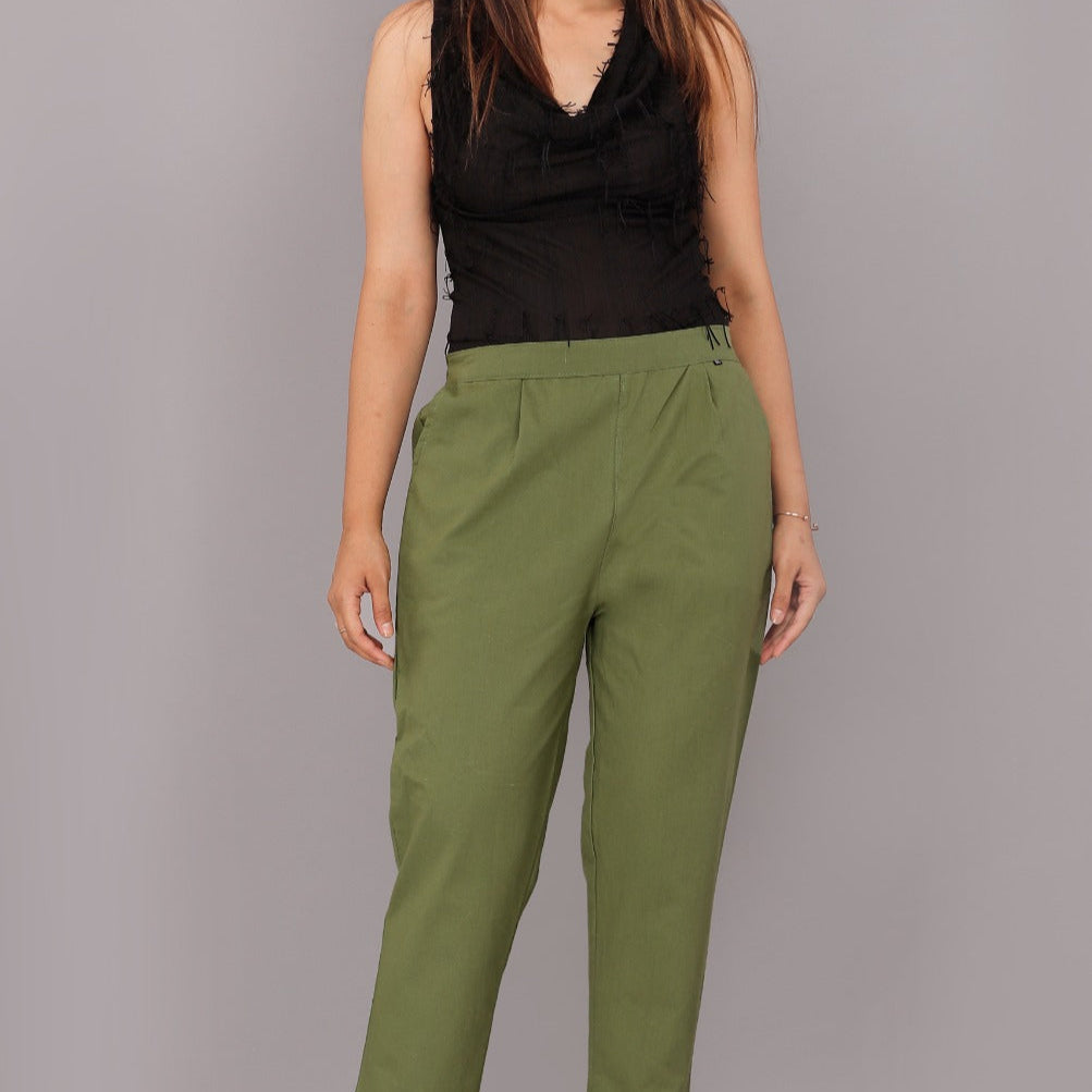 Woman wearing green pants and a black top on a gray background