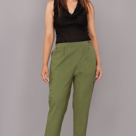Woman wearing green pants and a black top on a gray background